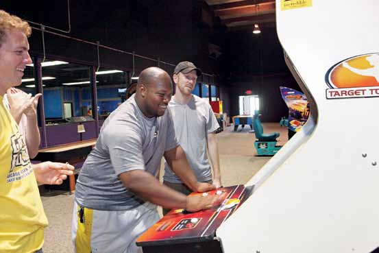 Galactic Fun Zone owner Lorenzo Williams takes a break to enjoy an arcade game while Adam Schussler looks on.