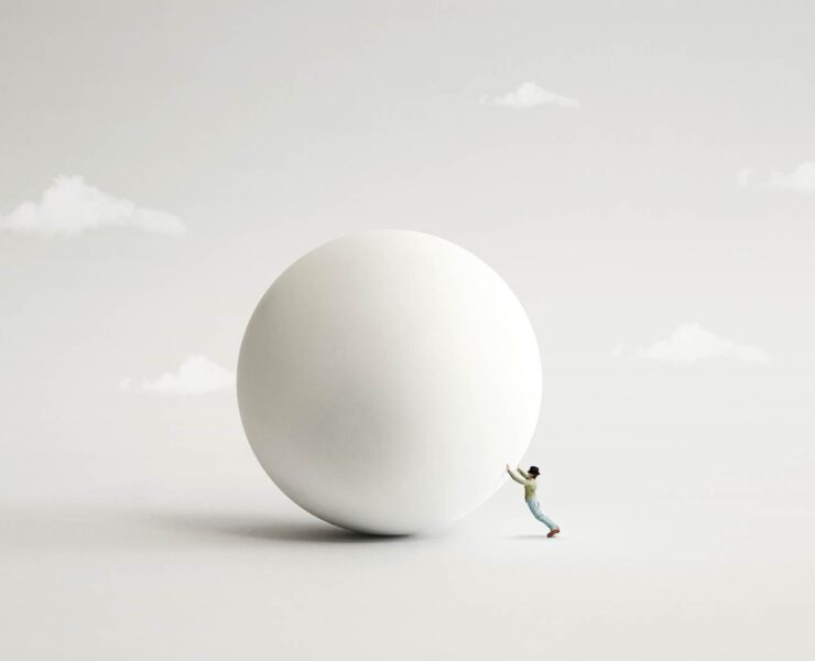 Surreal image of a small man attempting to push a large white ball on a grey surface with illustrative clouds in the background