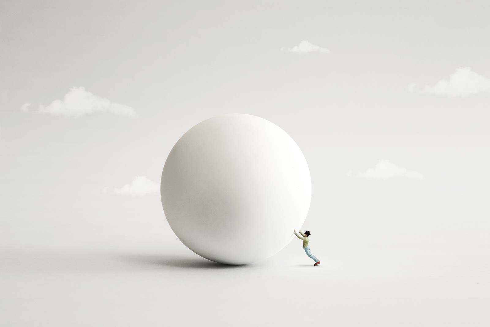 Surreal image of a small man attempting to push a large white ball on a grey surface with illustrative clouds in the background