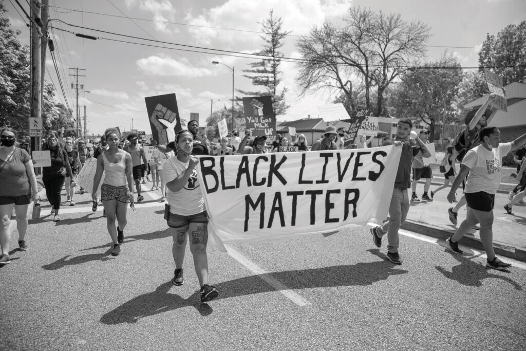 Black-Lives-Matter-Protest-two-black-women-carry-a-sign-saying-Black-Lives-Matter-hundreds-of-people-march-around-them