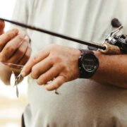 close up shot of a fishing rod and reel resting against a mans hands as he places bait on the hook