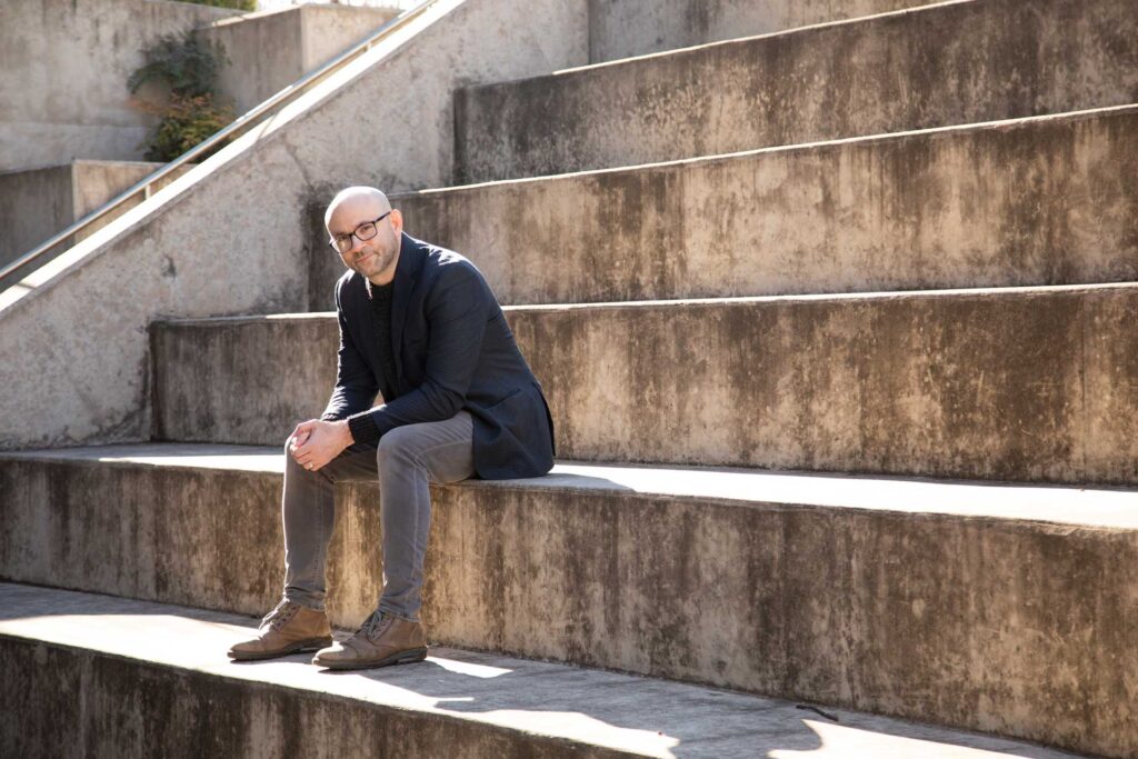 Headshot of a man named Robert Greene sitting on concrete steps