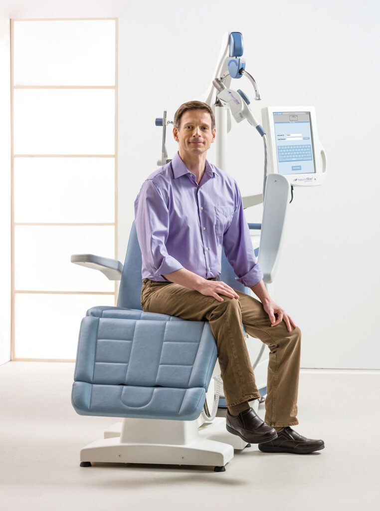 a male patient casually sitting in a medical grade patient chair against stark white walls