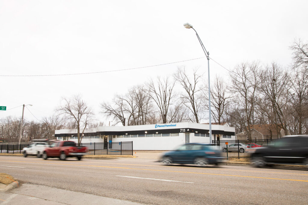 view across a busy road looking at a small building with the sign in blue text that says 