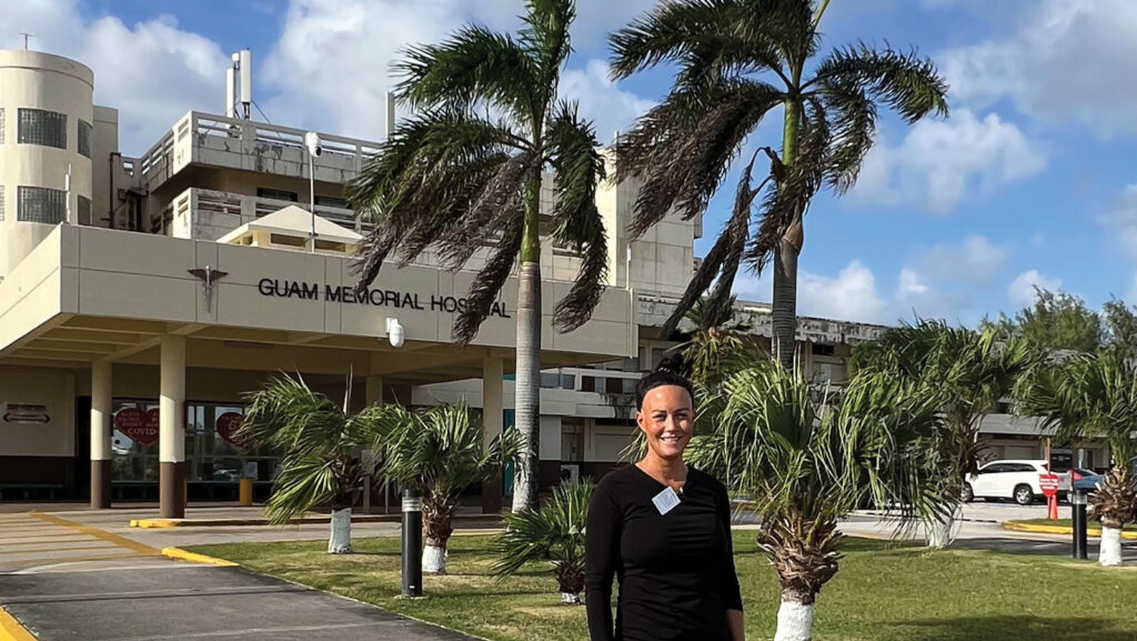 close up of a women stands in front of several palm trees outside a of hospital