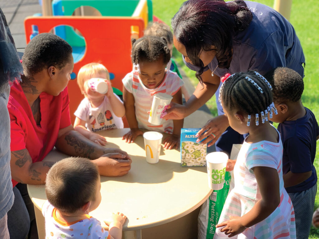 Two teachers with little kids gathered around a small table outside