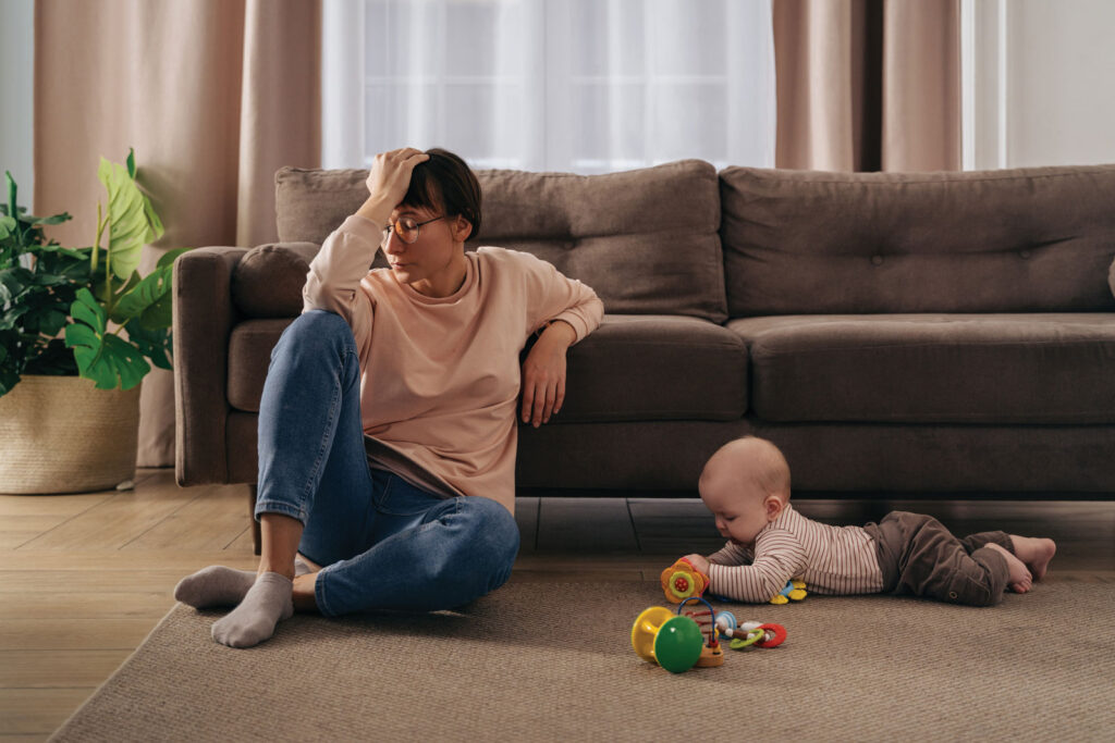 women resting in front of a couch on the floor with a baby playing besides her