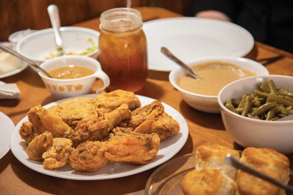 view of a wooden table filled with homestyle food such as fried chicken, green beans, sweet tea, gravy, and more