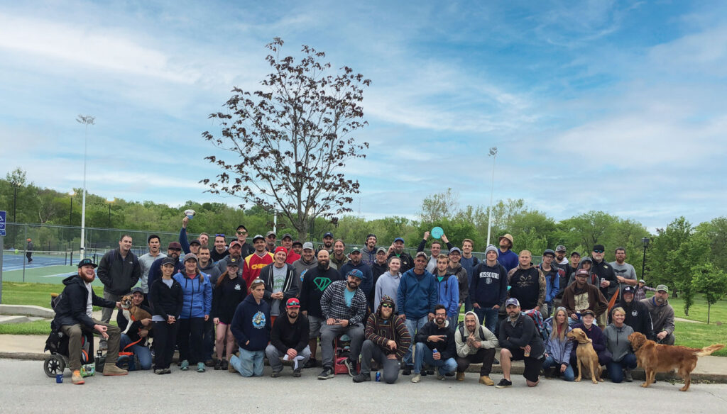 A large group of mostly men belonging to the Columbia Disc Golf Club in a park