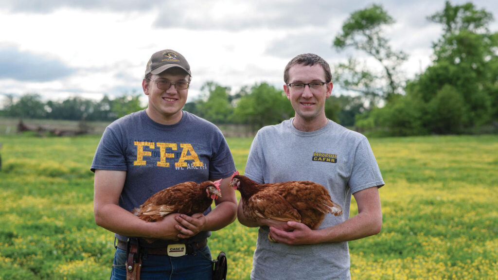 farmers and brothers named Dustin and Austin Stanton holding chickens stand in a field