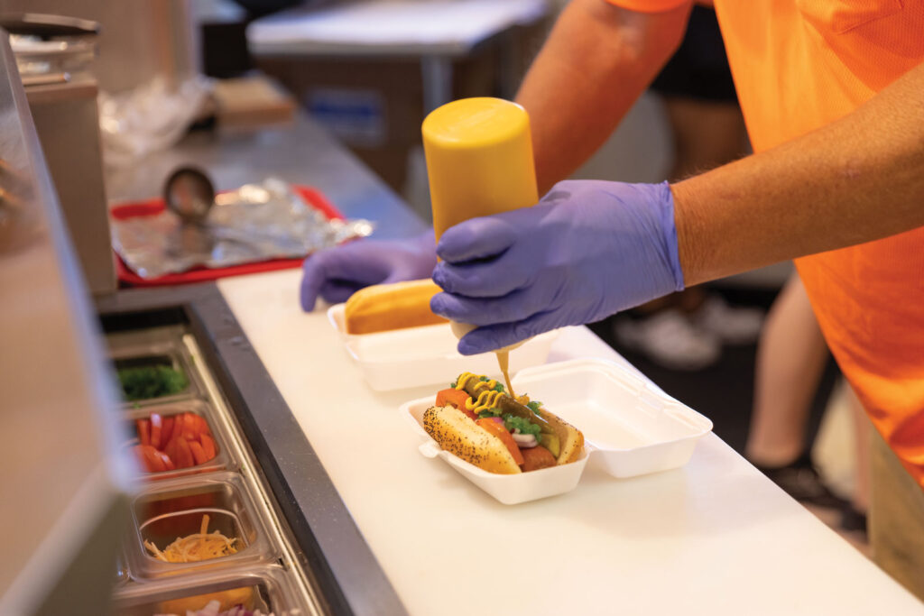 A chef tops a chili dog with mustard