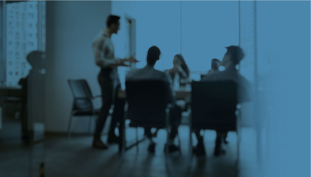 A blurry view of a group of people at a board meeting with one presenter speaking