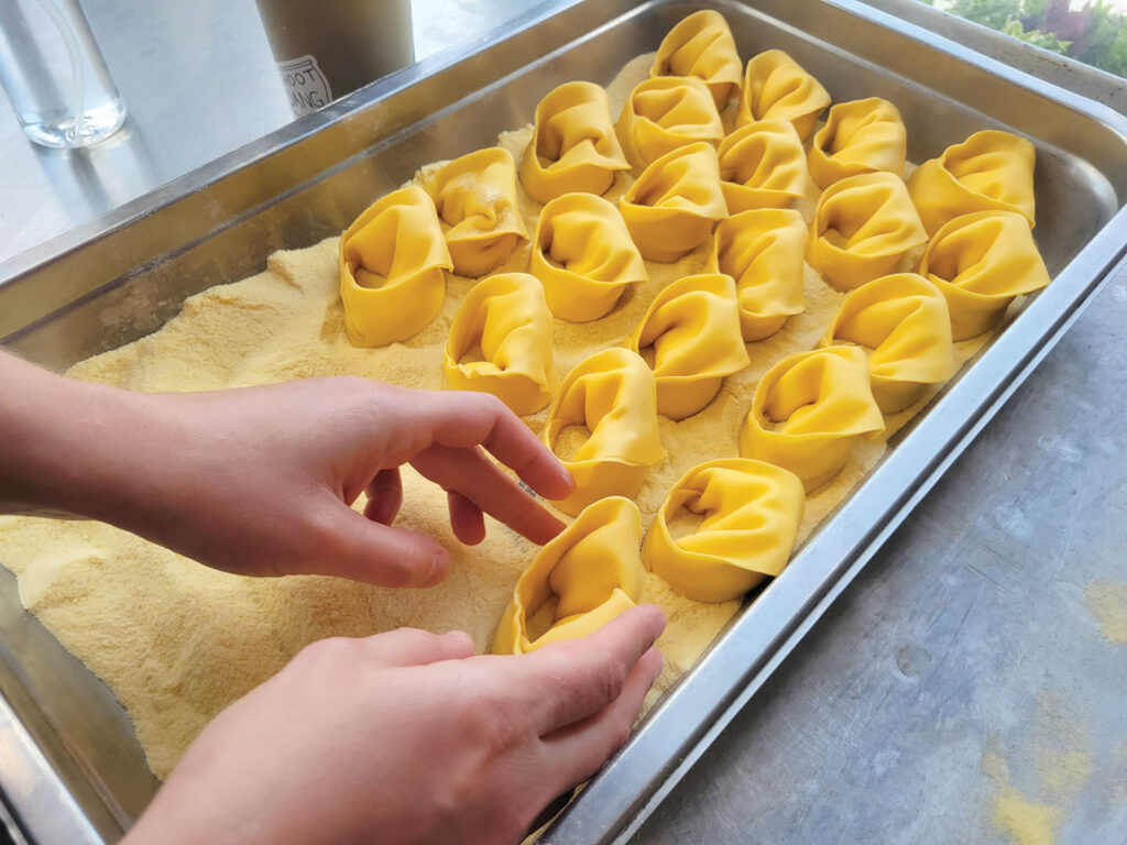 Close up of a employee making handmade pasta by hand in a mental tray