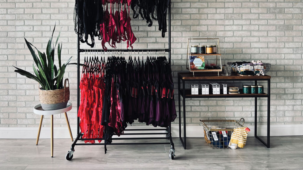 View of filled rack of clothes alongside stocked shelves against at a brick wall at a boutique