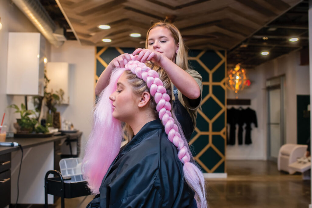 cosmetologist Kylie Phillips braiding a models hair with pink hair