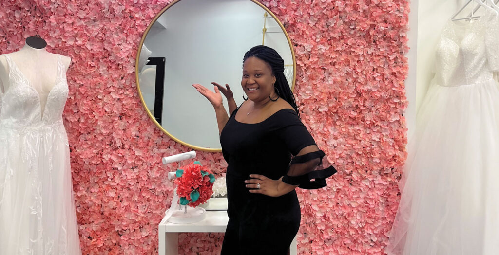 Owner of Stars Brides, Stars Simmons poses alongside a rack of bridal gowns