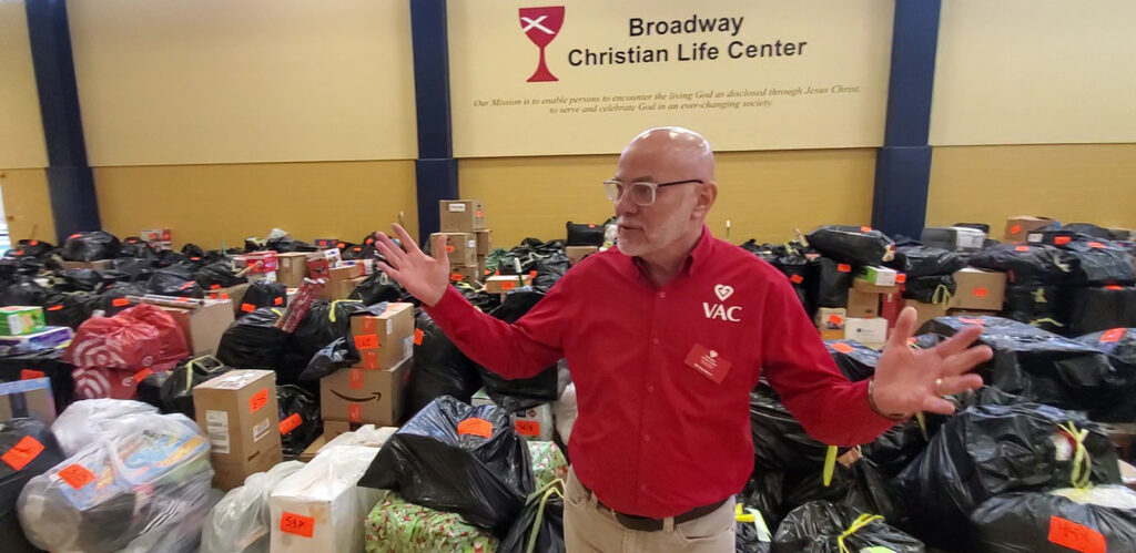 Ed Stansberry, executive director for Voluntary Action Center, gestures to show just a portion of the bagged gifts donated by businesses and community members.
