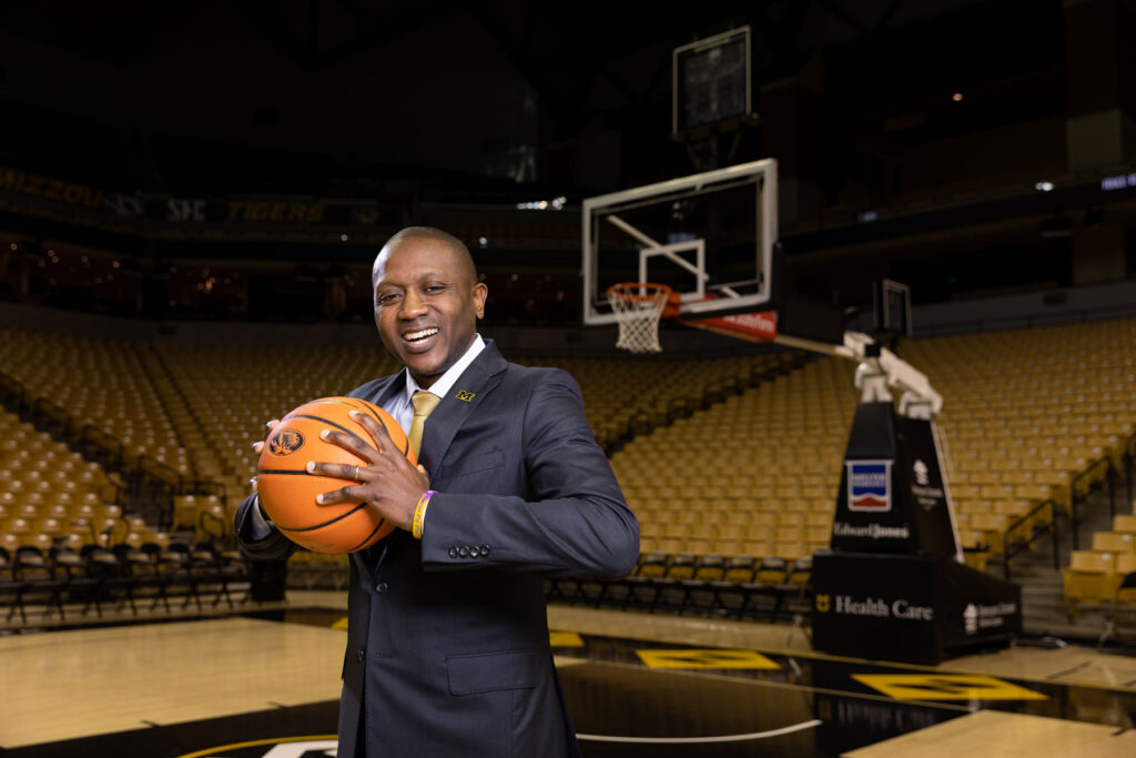 headshot of a smiling Dennis Gates, Mizzou basketball coach holding a basketball on the basketball court