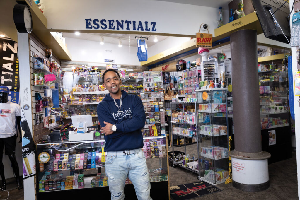 exterior view of stocked shelves of Essentialz business with owner Dimetrious Woods posing in the foreground