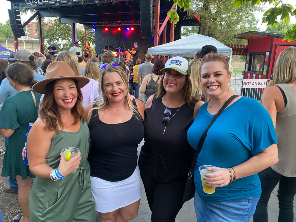 four women pose outside at the Rose Music Hall with artists preforming on stage in the background