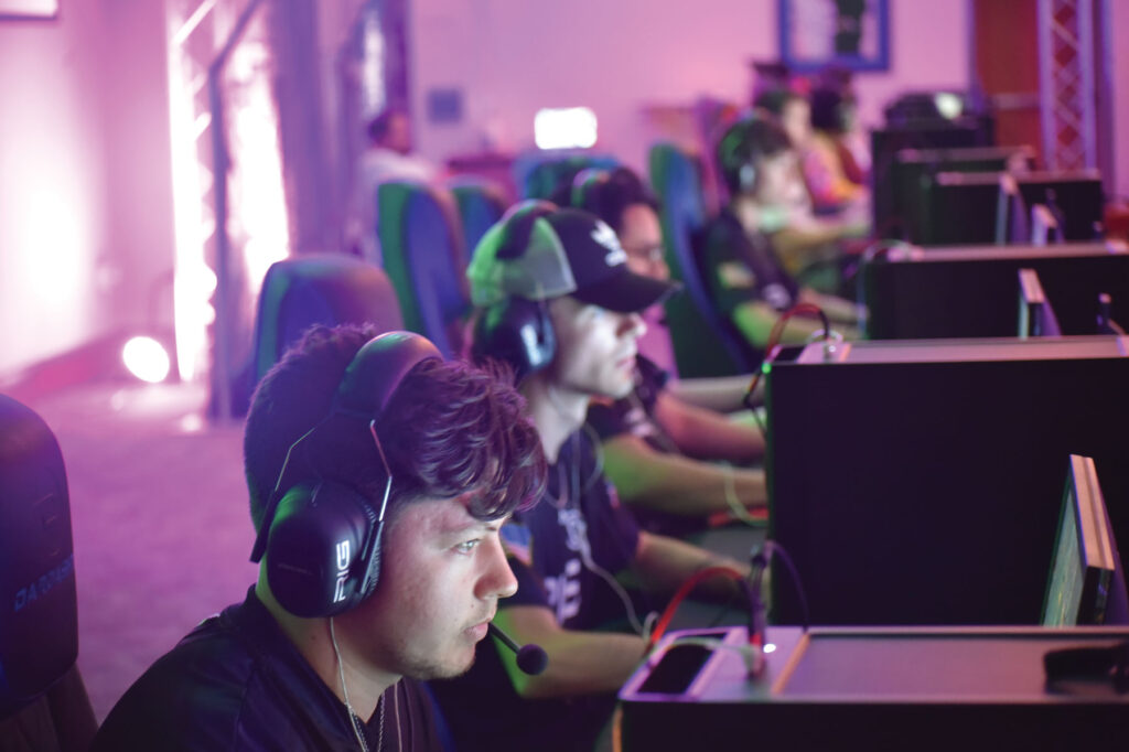 line of e sports players focused on their individual monitors and communicating through headsets