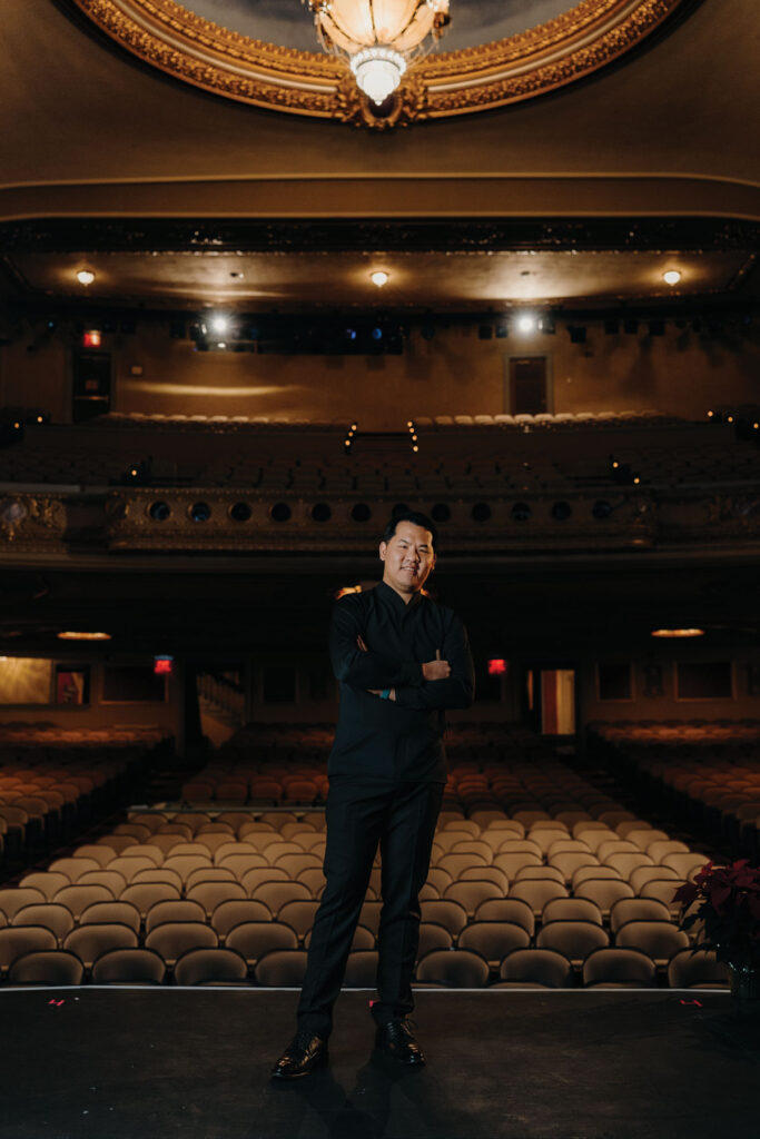 Headshot of conductor Wilbur Lin inside of a darked auditorium