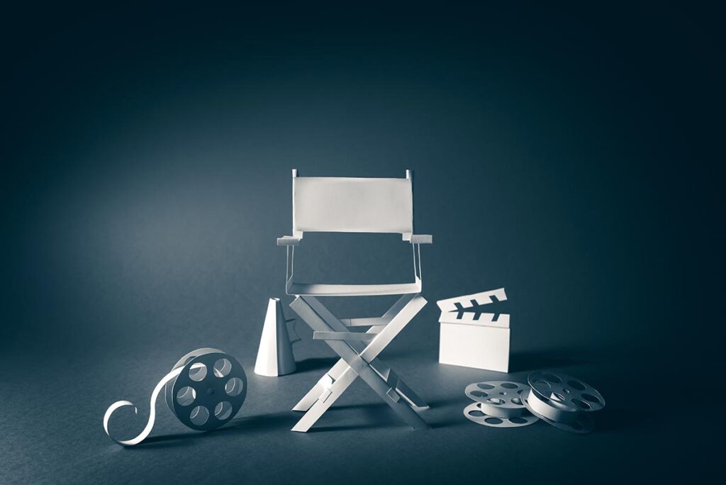 image of a chair made out of paper with film reels, a megaphone, and a director's cut board all made out of paper laying next to it