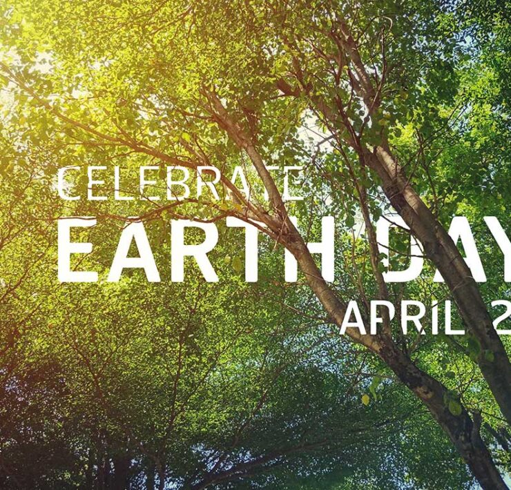 Celebrate Earth Day April 22 shows through the sunlight beaming through leaf-covered tree branches.