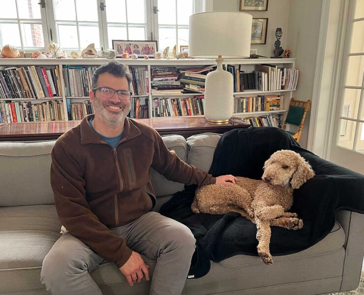 John Evelev relaxes on his sofa with his Goldendoodle Teddy.