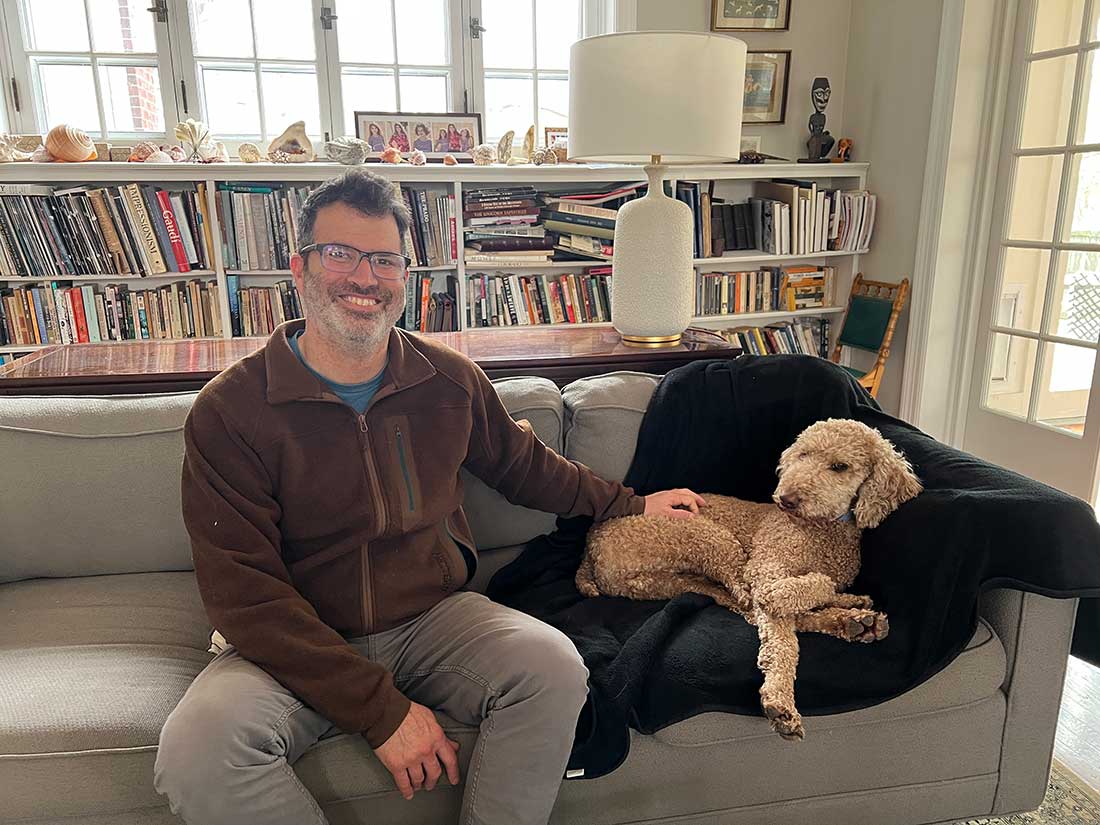 John Evelev relaxes on his sofa with his Goldendoodle Teddy.