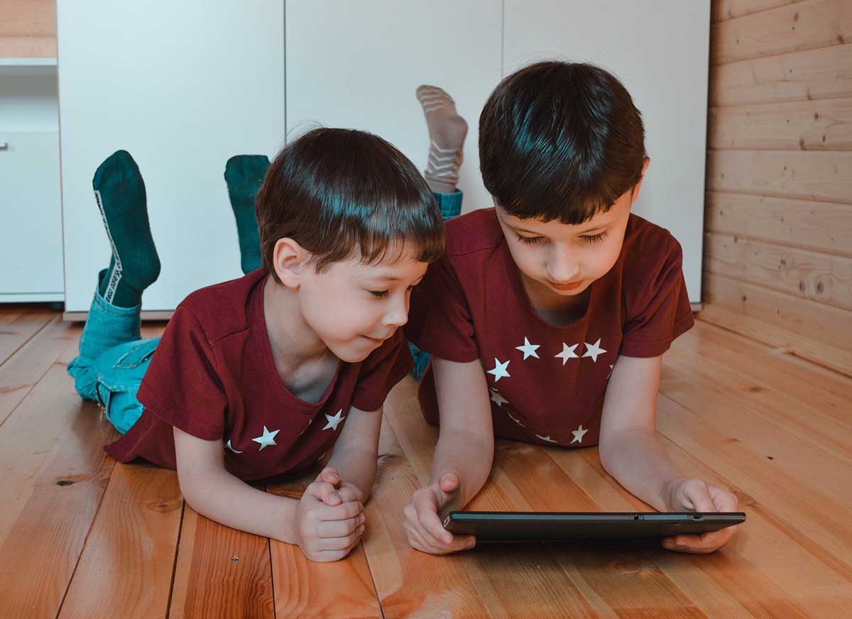 Two young boys are looking at the digital tablet to illustrate this article about online internet safety for kids.