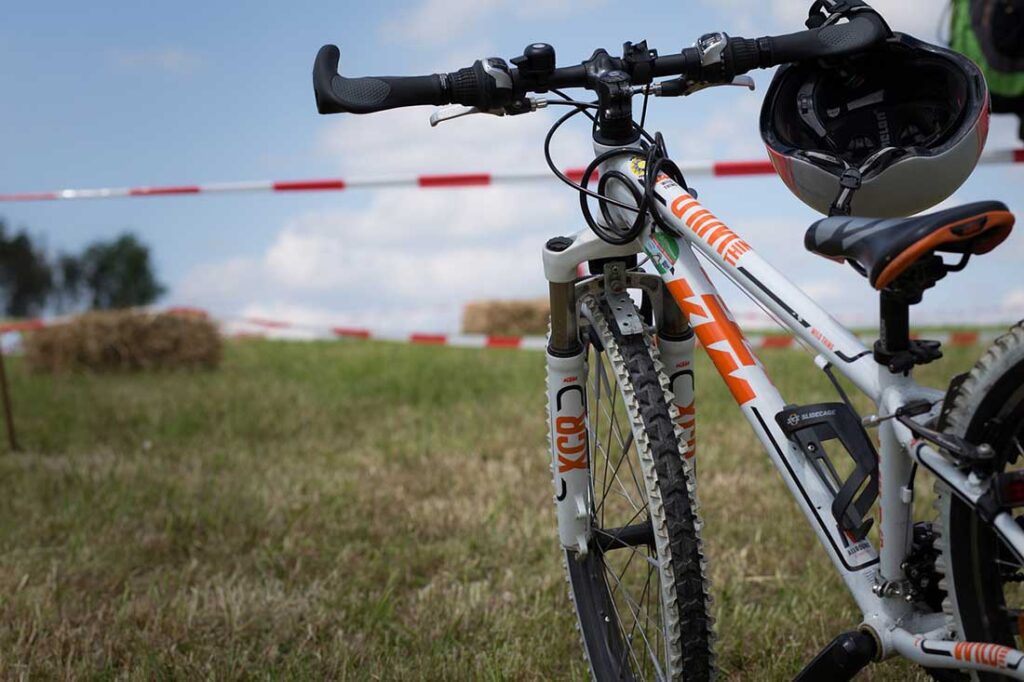 Image of a bicycle in the foreground at right center, with a cycling helmet looped around the right handlebar, and a trail awaits in the background.