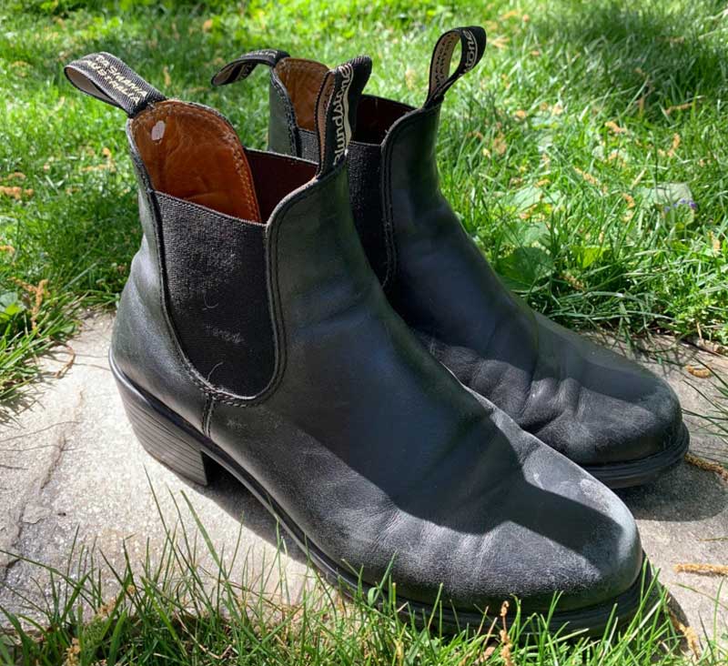 A pair of Blundstone boots are shown set on a rock with a grassy surrounding.