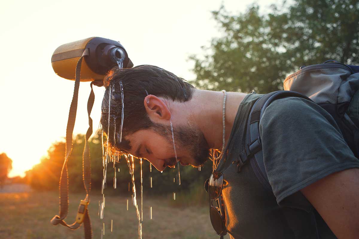 A hiker pours water on his head from a canteen to cool off.