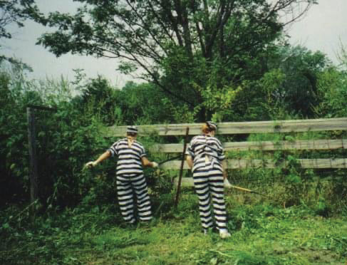 Kim Ambra and her sister doing chores in classic black and white striped prisoners costumes.