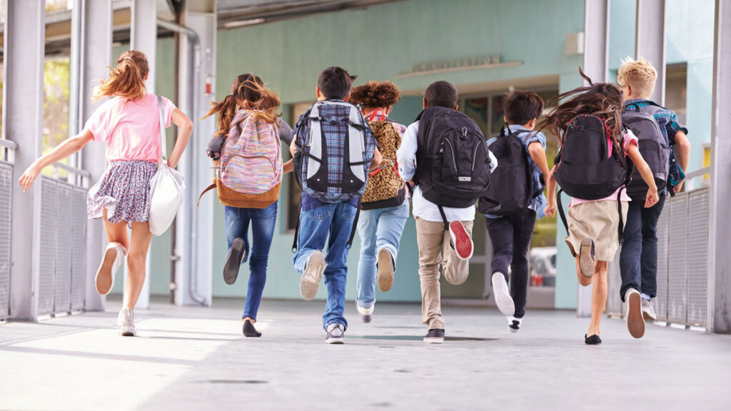 Group of school children running through walkway with backpacks and lunch sacks.