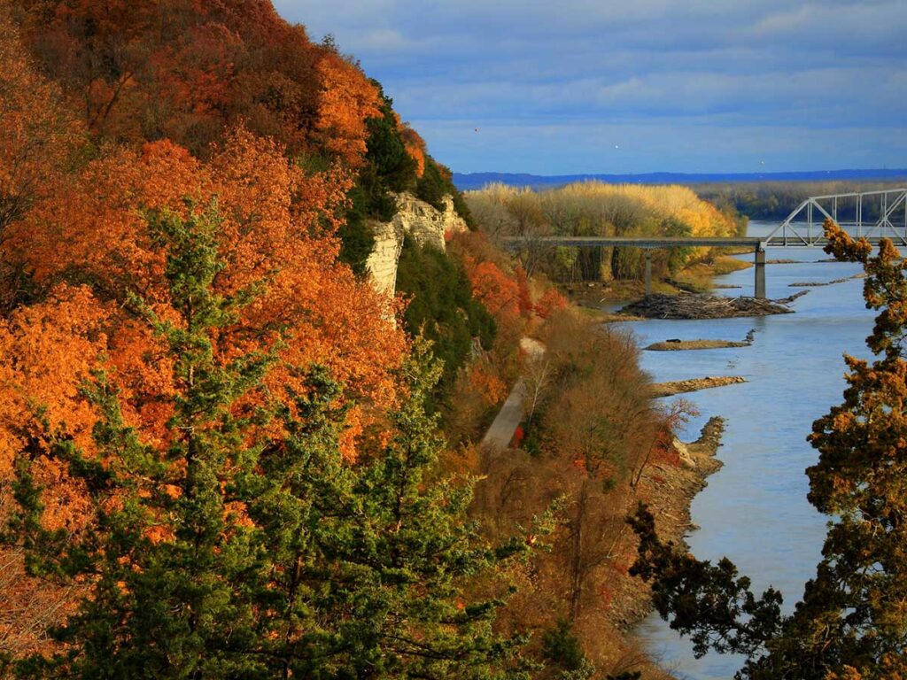 The Missouri River bluffs near Rocheport, Missouri, are full of color in the autumn photograph. The bluff is on the left, the Katy Trail runs along the side, and on the right is the Missouri River.