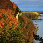 The Missouri River bluffs near Rocheport, Missouri, are full of color in the autumn photograph. The bluff is on the left, the Katy Trail runs along the side, and on the right is the Missouri River.