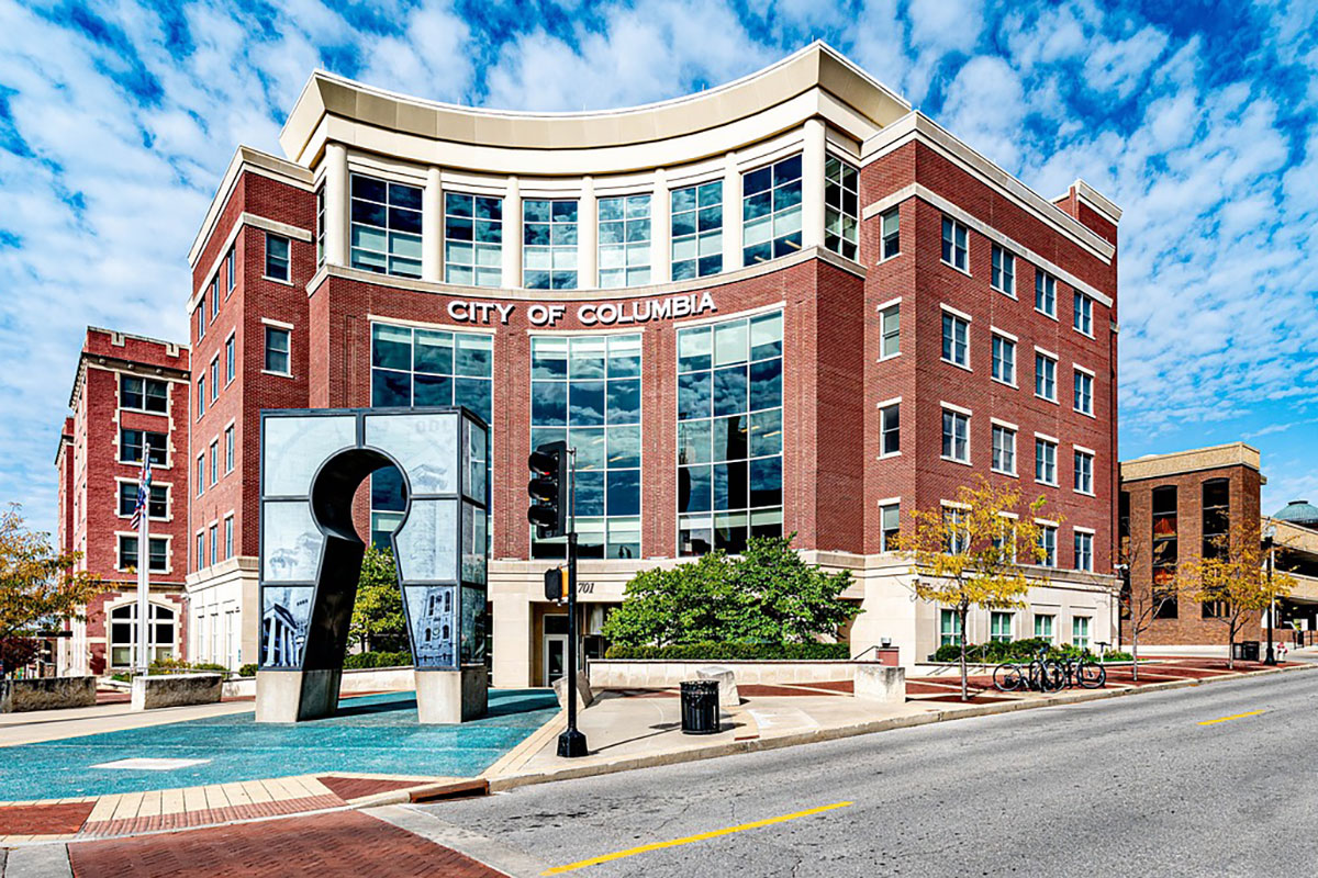 The Columbia, Missouri City Hall building, highlighted by high, pillowy clouds against a blue sky.