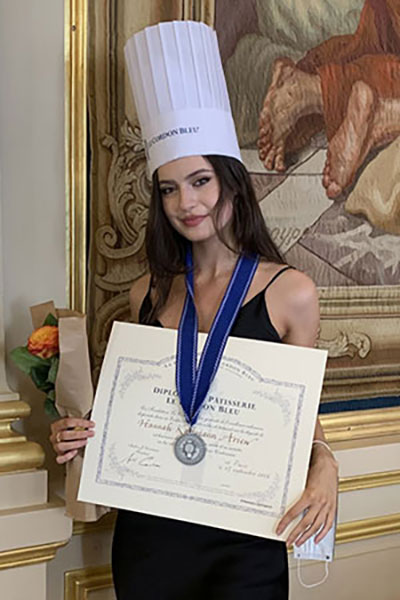 Hannah Sarina wearing a chef's hat and holding her culinary arts certificate.