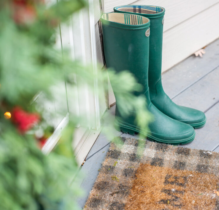 Green boots sit next to a welcome mat outside the back porch door