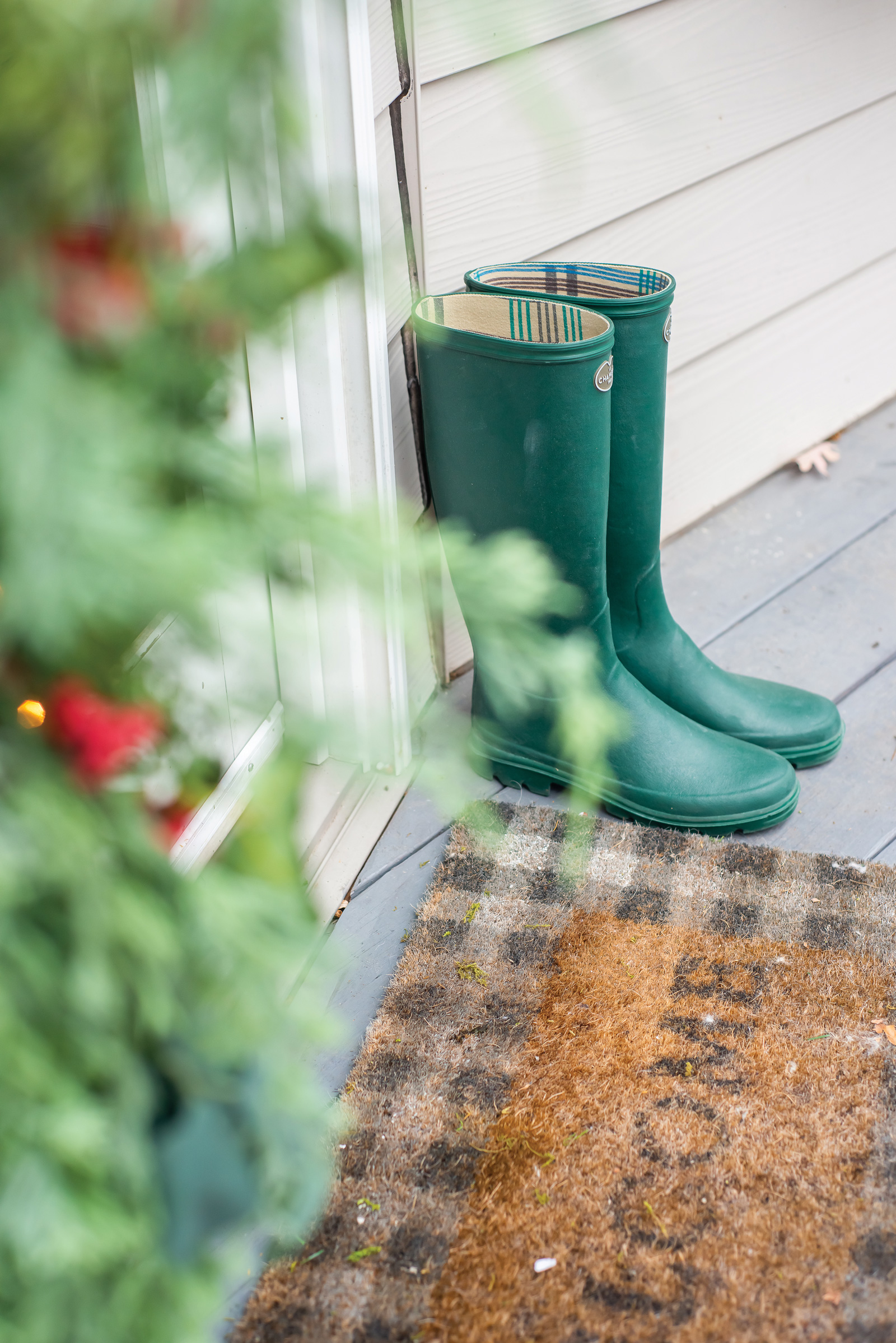 Green boots sit next to a welcome mat outside the back porch door