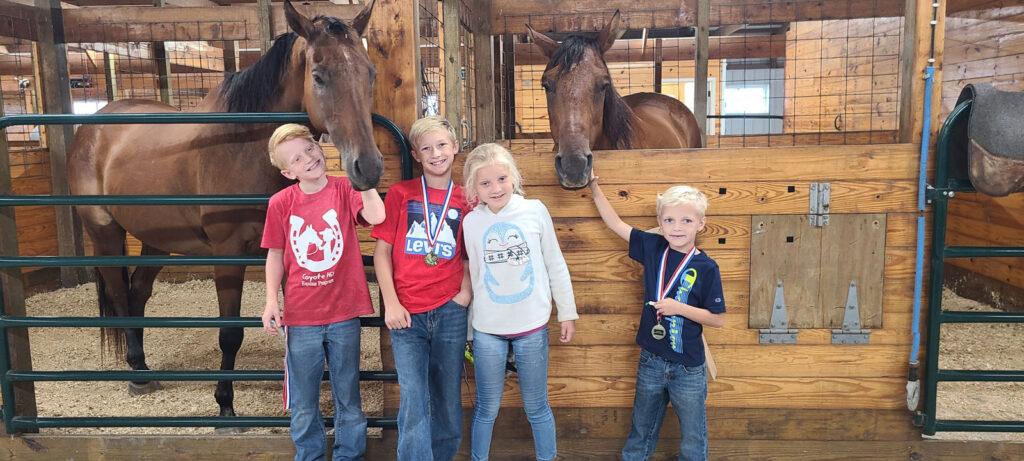 Coyote Hills students with medals patting horses in their stalls.