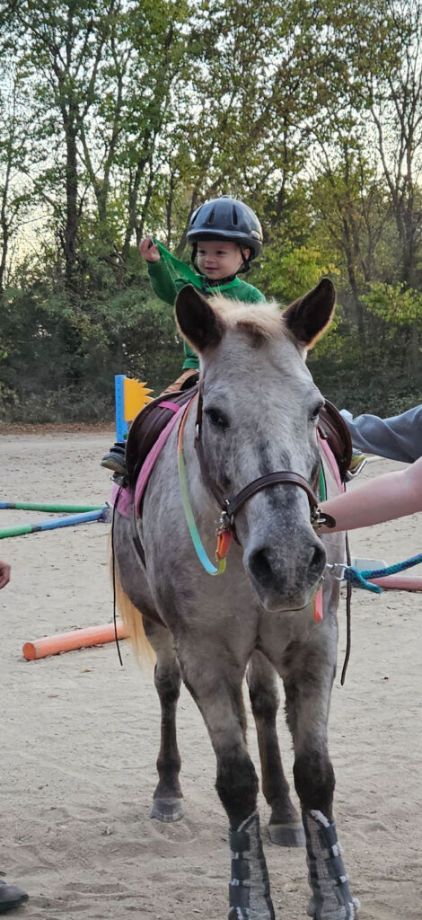 A Sunny Oak toddler-aged rider waving from the back of a horse. 