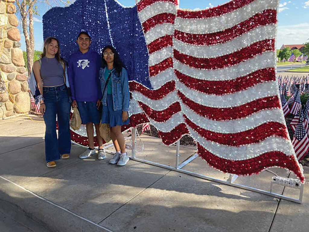 3 young exchange students stand in front of a US Flag.