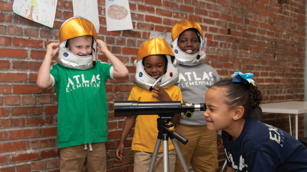 Students dressed as astronauts looking through telescope at Atlas Charter School