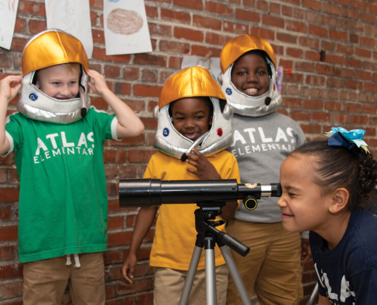 Students dressed as astronauts looking through telescope at Atlas Charter School