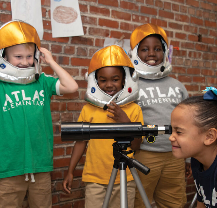 Students dressed as astronauts looking through telescope at Atlas Charter School