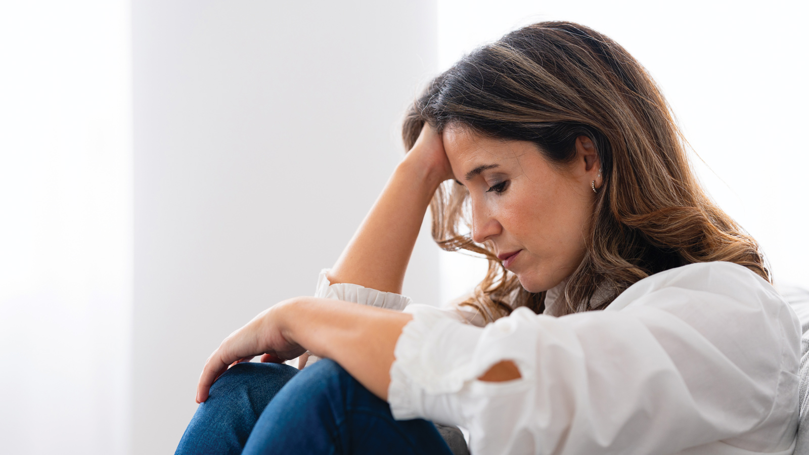 A Woman In A White Blouse Sitting And Resting holding her head