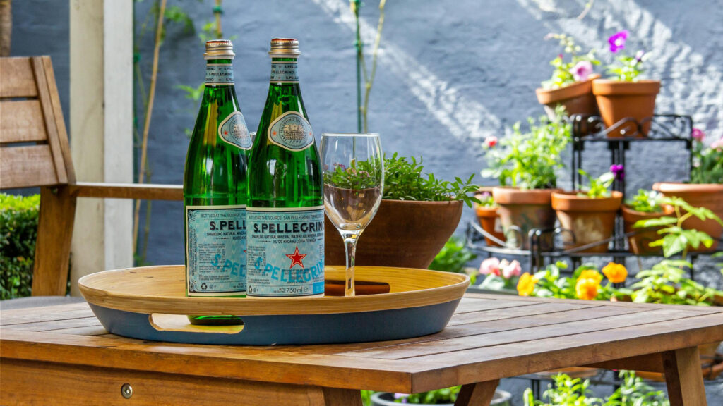 Featured Sparkling Water Sitting On A Table on an outdoor patio with flower pots in the background